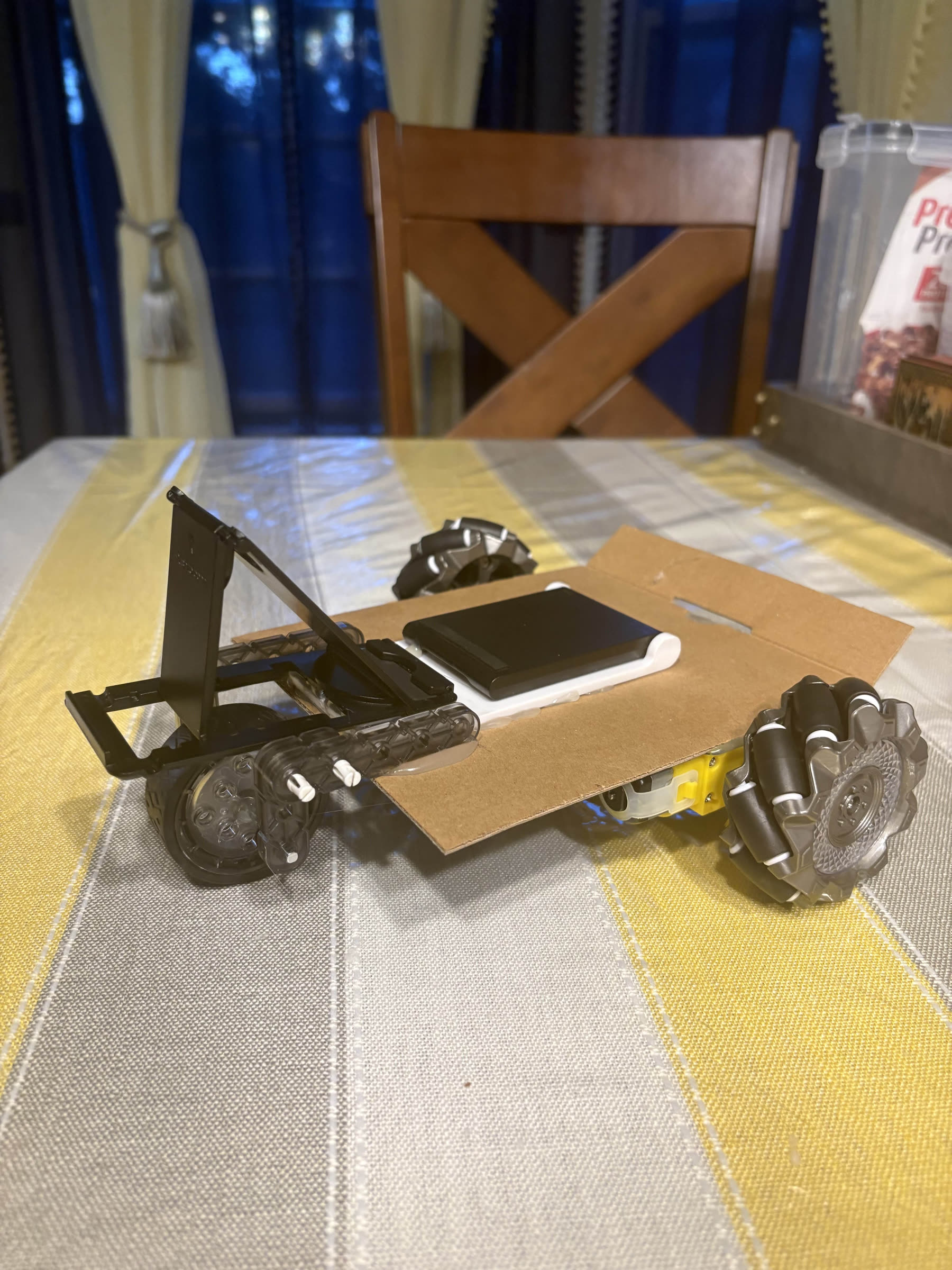 Early cardboard-and-household-materials prototype of the face-tracking phone mount, with a phone clamped to a mount on a wheeled chassis