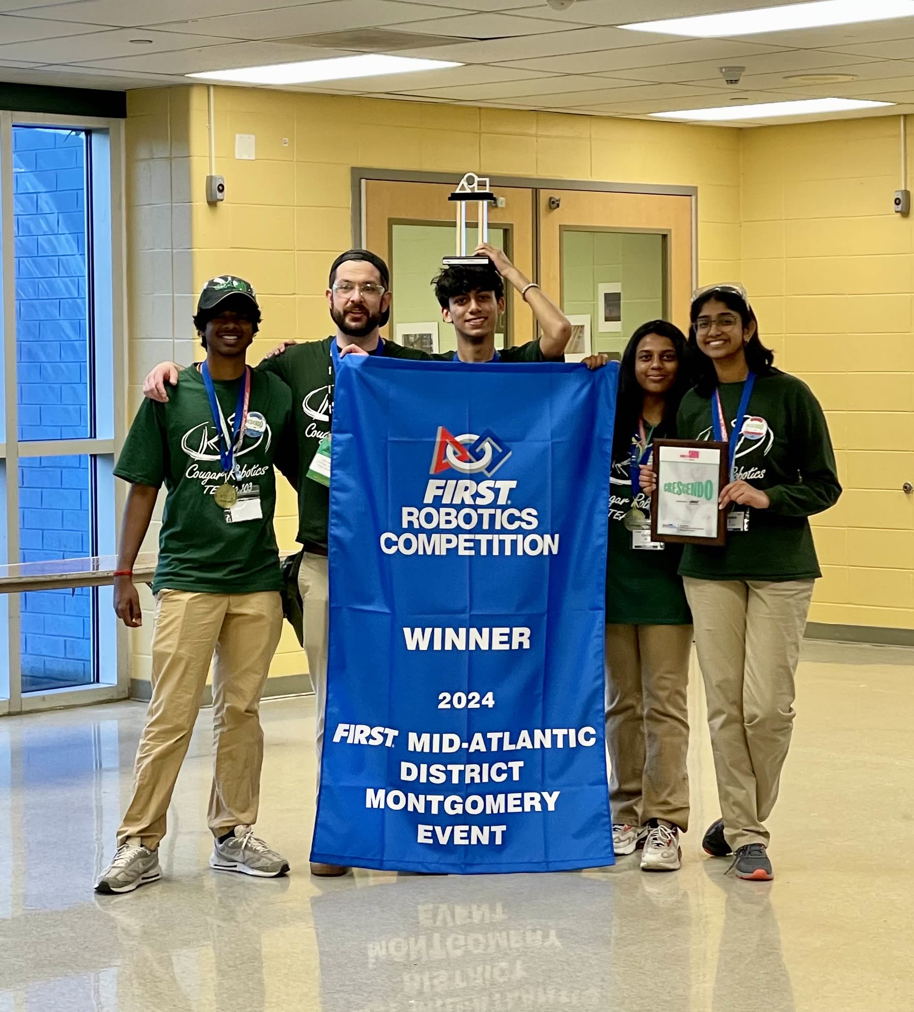 Team 1403's drive team holding the FIRST Robotics Competition District Event Winner banner and award plaque